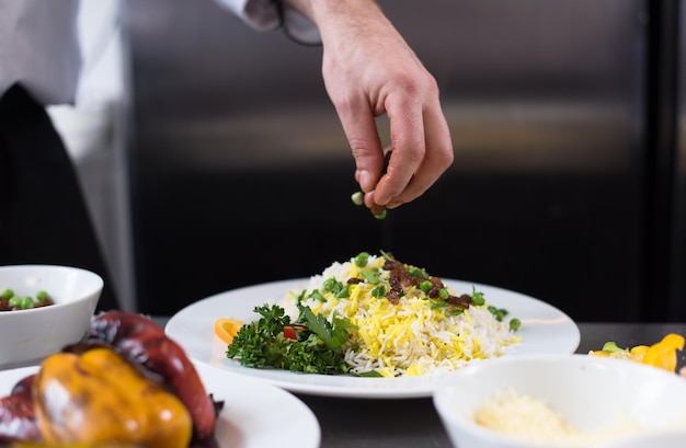 Mains de chef servant un risotto aux légumes dans la cuisine du restaurant