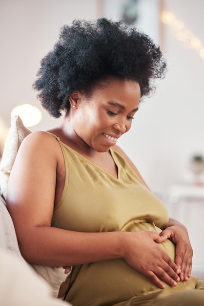 Mains de coeur enceinte et estomac de femme noire avec signe de la main sentiment d'amour de la mère Canapé de soins de maman et salon du salon avec une personne tenant l'abdomen heureuse de la grossesse et du bébé sur un canapé de la maison