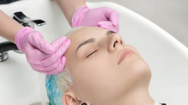 Mains de coiffeur dans des gants roses lavant la couleur des cheveux émeraude dans un salon de beauté professionnel.