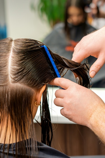 Mains d'un coiffeur peignant les cheveux d'une jeune femme