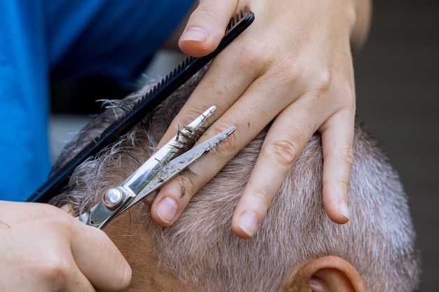 Les mains d'un coiffeur professionnel avec des ciseaux et un peigne peignent les cheveux d'un homme