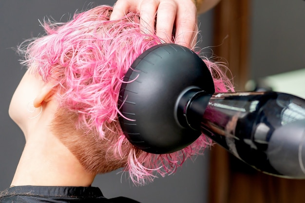 Mains de coiffeur sèche les cheveux roses de gros plan de femme.