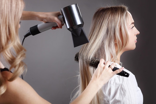 Mains de coiffeurs séchant les cheveux longs avec sèche-cheveux et brosse ronde