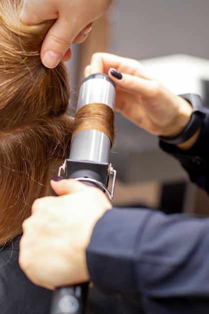 Les mains d'une coiffeuse bouclent le client de cheveux avec un fer à friser dans un salon de coiffure, se bouchent.