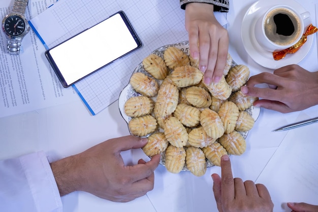 Mains de collègues de travail arabes mangeant eid kahk ensemble sur un bureau de travail