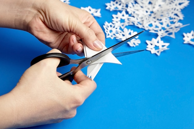 Mains coupant des flocons de papier blanc sur fond bleu