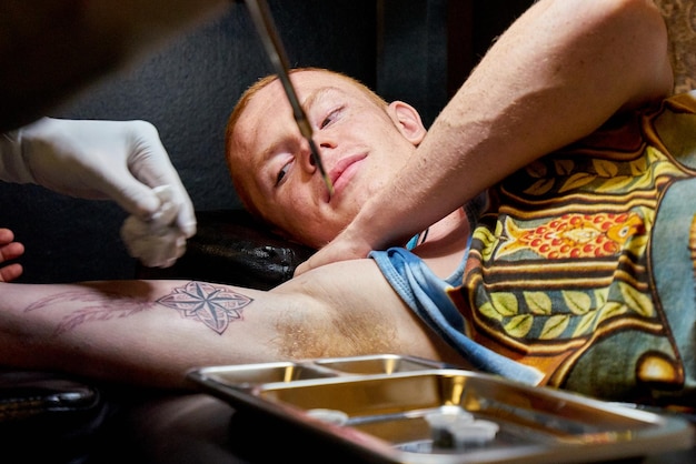 Des mains coupées d'un artiste tatouant du bambou sur le bras d'un jeune homme