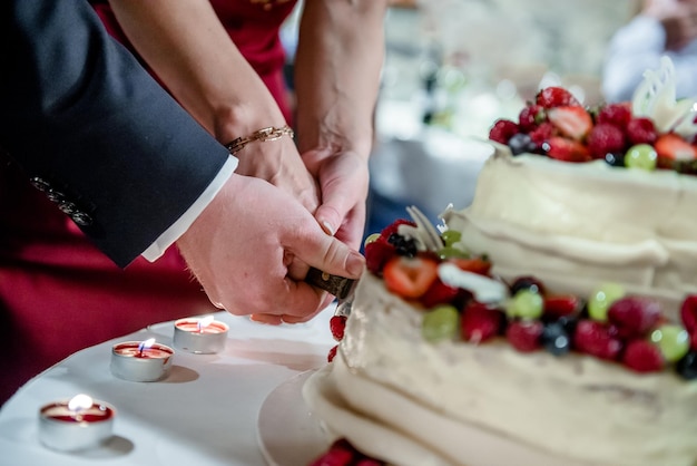 Photo des mains coupées d'un couple de jeunes mariés coupant un gâteau lors d'une cérémonie de mariage