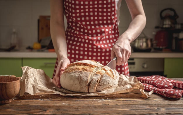 Mains coupées avec un couteau pain frais naturel fait maison avec une croûte dorée sur fond de bois Cuisson des produits de boulangerie