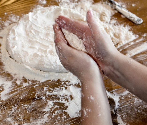 Des mains coupées sur un enfant aplatissant de la pâte sur la table