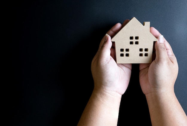 Des mains coupées d'un enfant tenant une maison modèle sur un fond noir