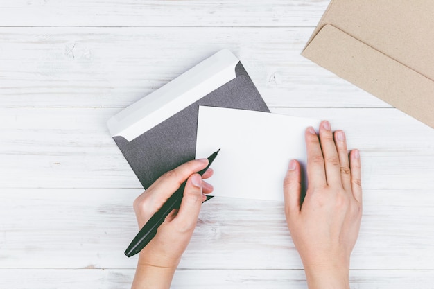 Photo des mains coupées d'une femme écrivant un message sur papier sur une enveloppe sur la table