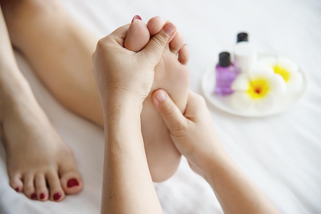 Des mains coupées d'une femme massant les pieds d'un client par des fleurs dans un spa