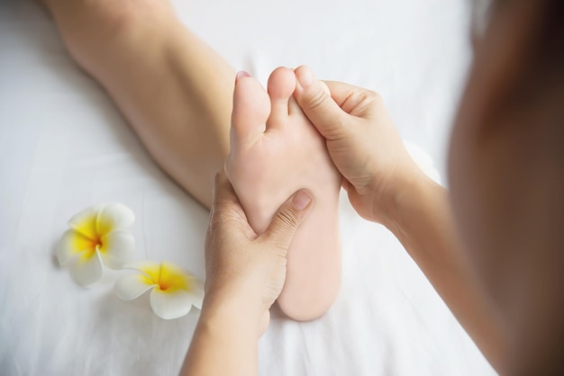Des mains coupées d'une femme massant les pieds d'un client par des fleurs dans un spa