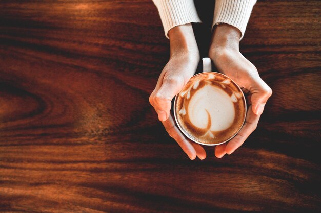 Photo des mains coupées d'une femme tenant du café à la table