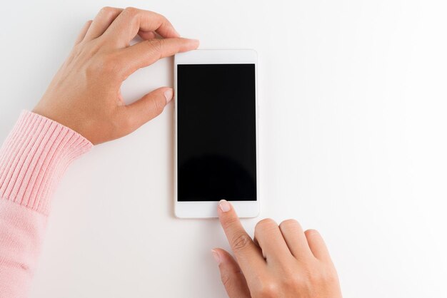 Des mains coupées d'une femme tenant un téléphone intelligent vide sur un fond blanc