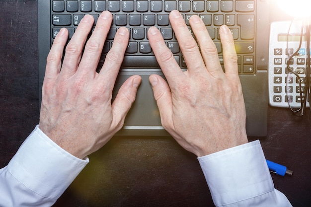 Photo des mains coupées d'un homme d'affaires utilisant un ordinateur portable à son bureau