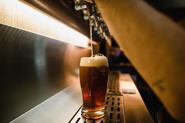 Photo des mains coupées d'un homme versant de la bière du robinet dans un verre