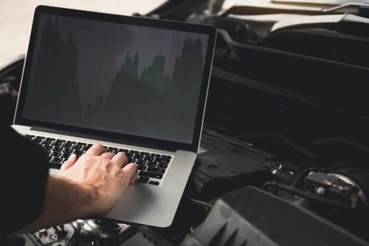 Photo des mains coupées d'un mécanicien utilisant un ordinateur portable sur un moteur de voiture