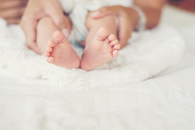 Des mains coupées d'une mère tenant les pieds d'un bébé sur le lit