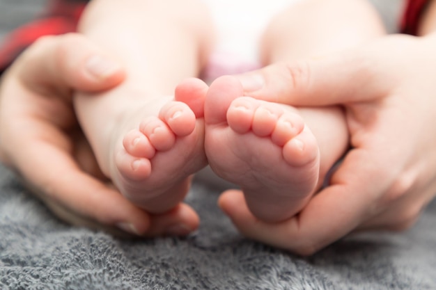 Des mains coupées d'une mère tenant les pieds d'un bébé sur le lit