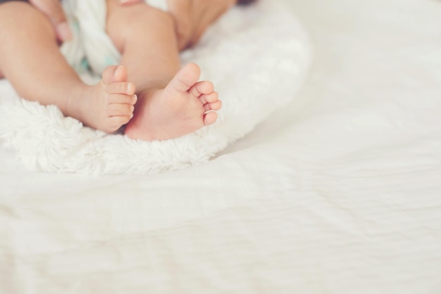 Des mains coupées d'une mère tenant les pieds d'un bébé sur le lit