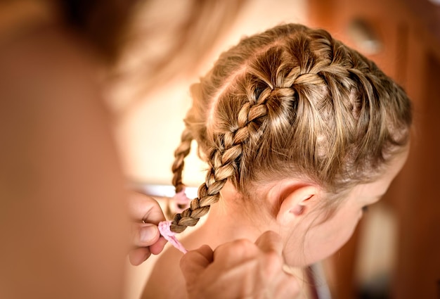 Photo des mains coupées d'une mère tressant les cheveux de sa fille.