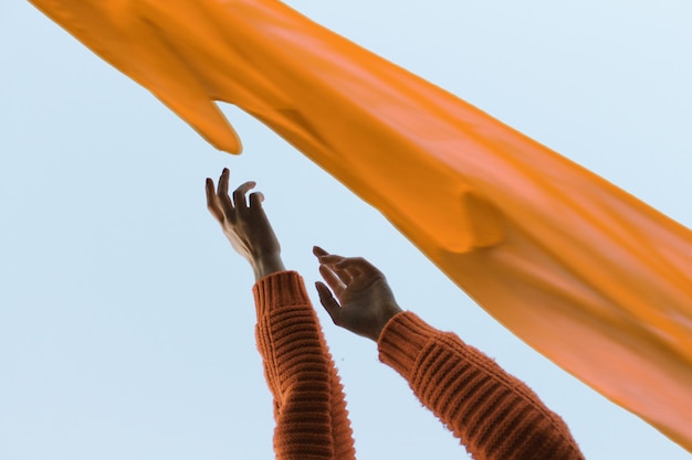 Des mains coupées par un textile orange contre un ciel clair