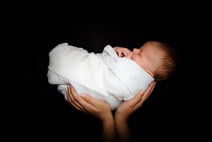 Photo des mains coupées d'un parent tenant un nouveau-né sur un fond noir