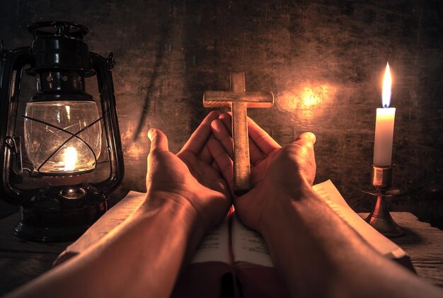 Photo des mains coupées d'une personne priant sur une bible et une croix religieuse