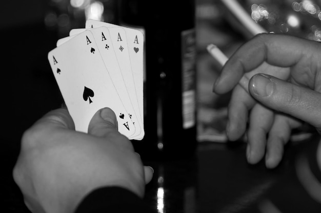 Photo des mains coupées tenant des cartes à jouer et une cigarette.