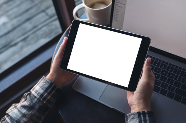 Photo des mains coupées tenant une tablette numérique par un ordinateur portable dans un café