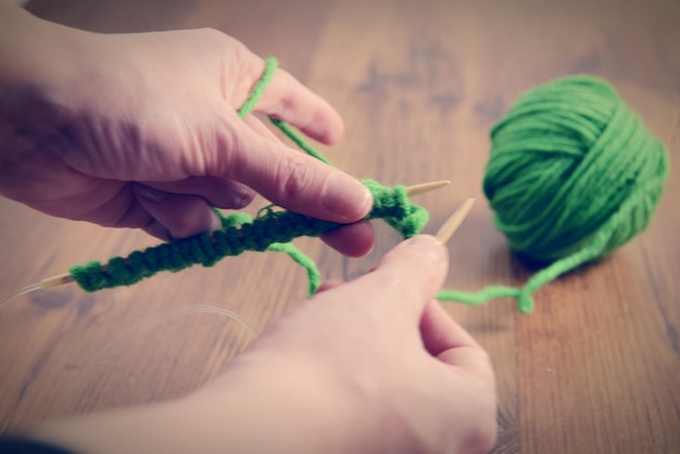 Des mains coupées tricotant de la laine verte sur la table à la maison.