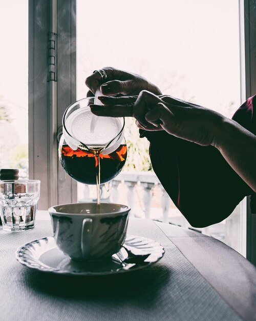 Photo des mains coupées versant du thé dans une tasse sur la table.