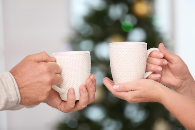 Mains d'un couple de personnes âgées heureux buvant du thé chaud à la maison. Notion de Noël