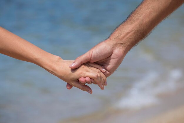 Mains de couple tenues ensemble près de l'eau de mer bleue sur le fond de la plage se bouchent