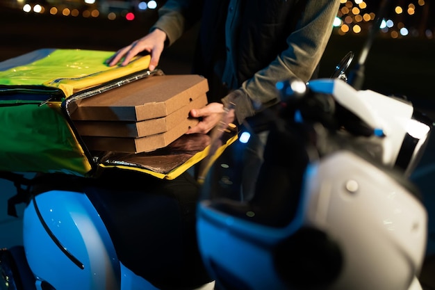 Les mains d'un coursier qui sort des boîtes de pizza d'un sac Livraison de nourriture en soirée