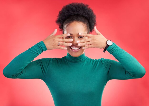 Photo les mains couvrent le visage et la femme en studio avec cachette et les yeux culminent avec un sourire femme africaine sur fond rouge et heureuse du secret et du modèle de chicago avec annonce de potins et portrait