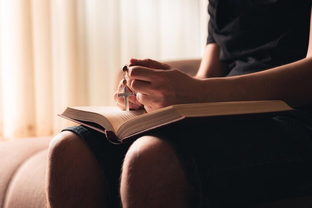 Mains d'un croyant avec une sainte bible et une croix dans ses mains