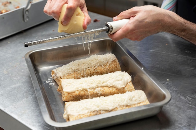 Les mains d'un cuisinier méconnaissable râpant du fromage sur des crêpes