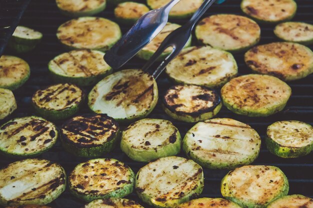 Les mains des cuisiniers retournent des courgettes grillées pinces métalliques sur fond de délicieuses courgettes à la croûte délicieuse.