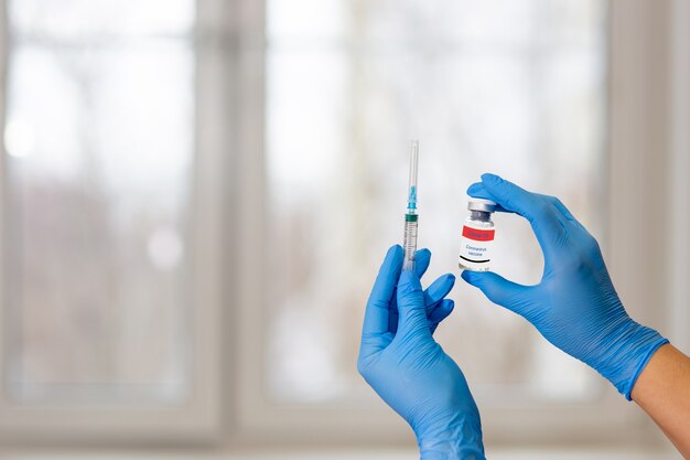 Les mains dans des gants bleus tiennent un flacon de vaccin COVID-19 avec une seringue.