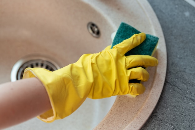 Mains dans des gants jaunes nettoyant un évier avec une éponge