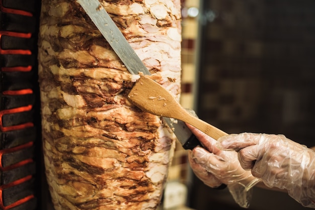 Mains dans des gants jetables coupant la viande sur une brochette