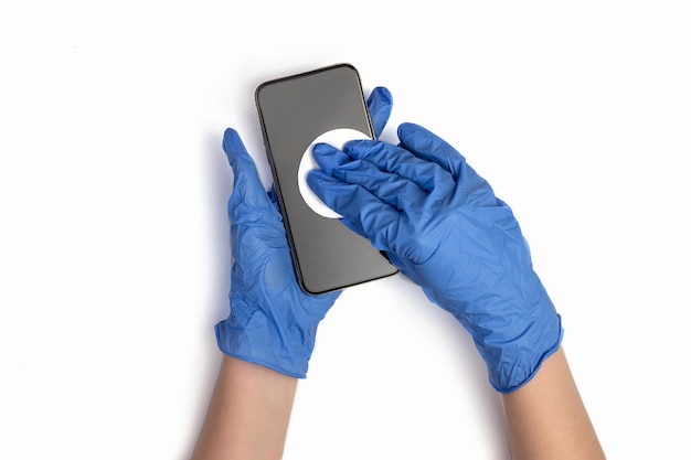 Mains dans des gants médicaux essuyez l'écran du smartphone avec un chiffon désinfectant Gros plan des mains nettoient le téléphone portable isolé sur fond blanc Désinfection du smartphone