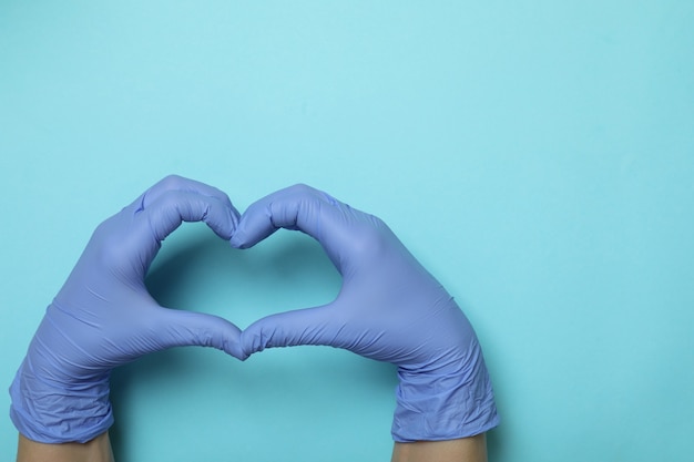 Mains dans des gants médicaux montre coeur sur fond bleu isolé