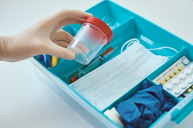 Les mains dans des gants médicaux prennent la tasse d'essai de la boîte de médecine. Concept de soins de santé et de médecine. Trousse de premiers secours