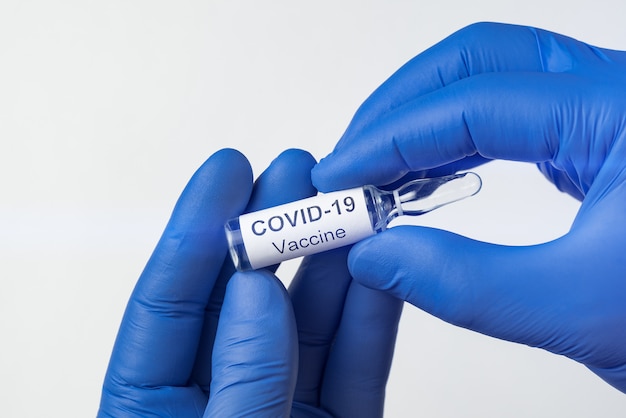 Mains dans des gants médicaux tenant une ampoule de coronavirus vaccin. Flacon avec étiquette Covid-19