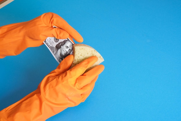 Les mains dans des gants orange lavent l'argent avec du savon et une éponge sur fond bleu