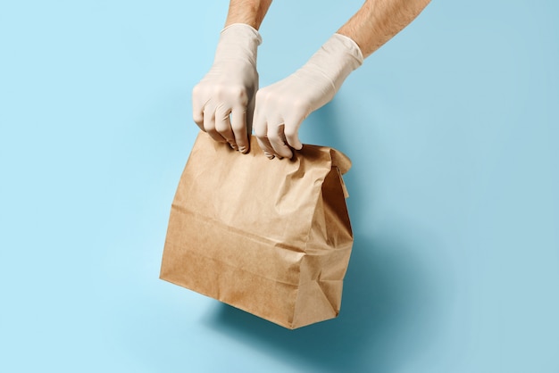 Les mains dans des gants de protection tiennent le paquet d'artisanat sur un mur bleu avec un espace de copie.